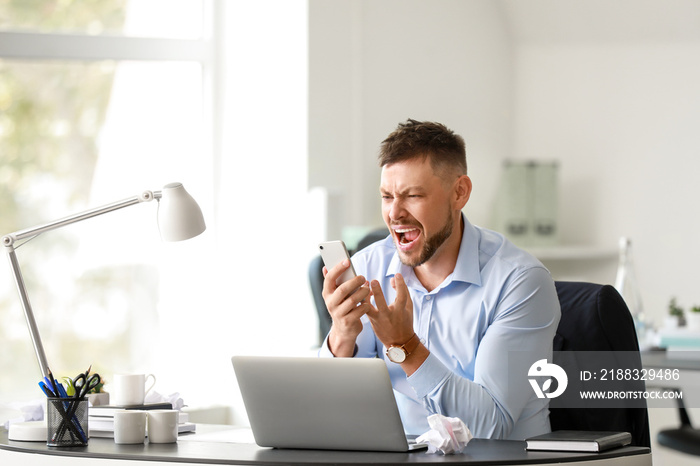 Stressed man talking by mobile phone at table in office