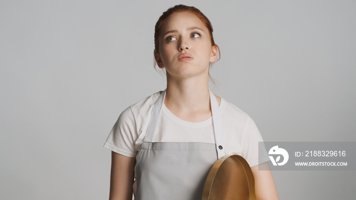 Attractive waitress in apron with tray thoughtfully looking away over white background