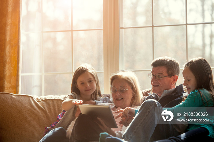 Grandparents with grandchildren (2-3, 10-11) sitting on sofa and using tablet pc