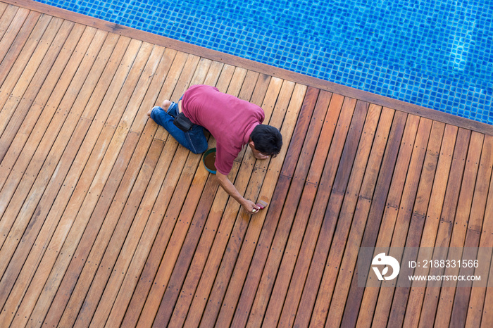 一名男子在室外木制游泳池甲板上作画，俯视图