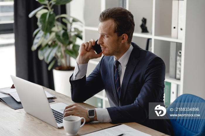 Calm man with laptop in the office having phone conversation