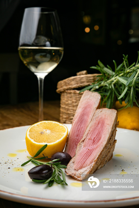 Grilled tuna with lemon, greens and olives on a plate. On a wooden table