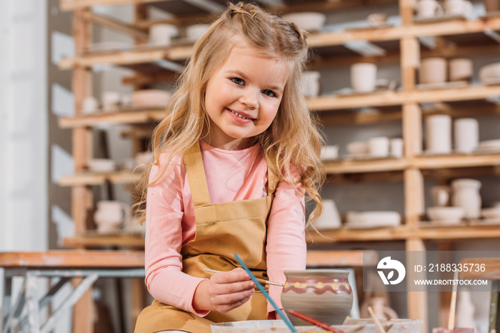 smiling child painting ceramic pot in workshop