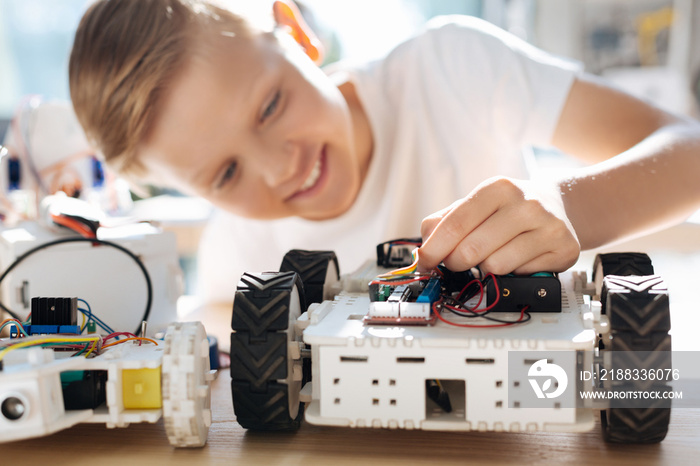 Fair-haired boy adjusting wires in robotic car