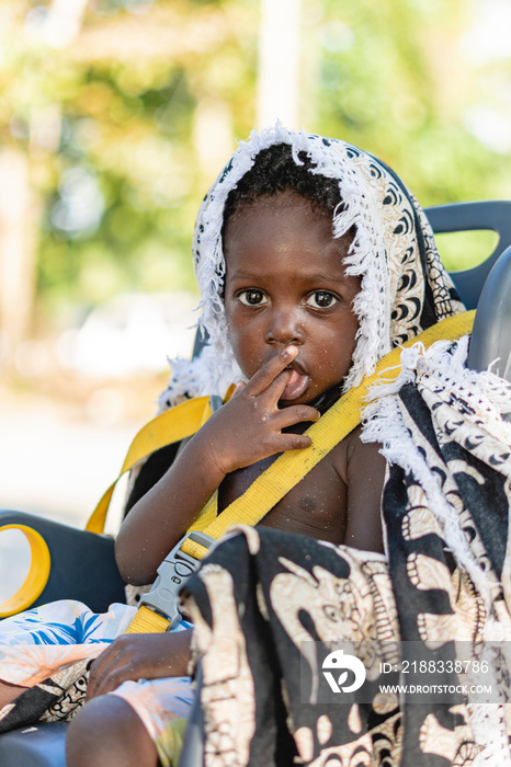 Retrato vertical de un niño afroamericano mirando seriamente a cámara con su dedo metido en la boca 