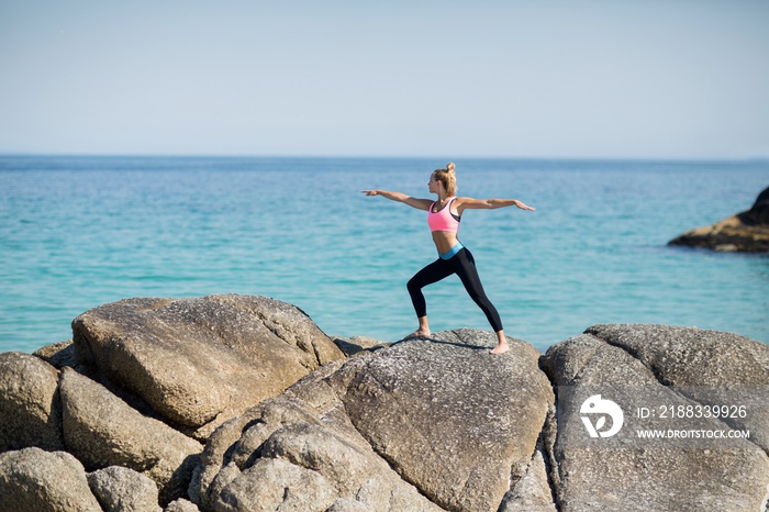 Woman practicing warrior pose on rocky shore