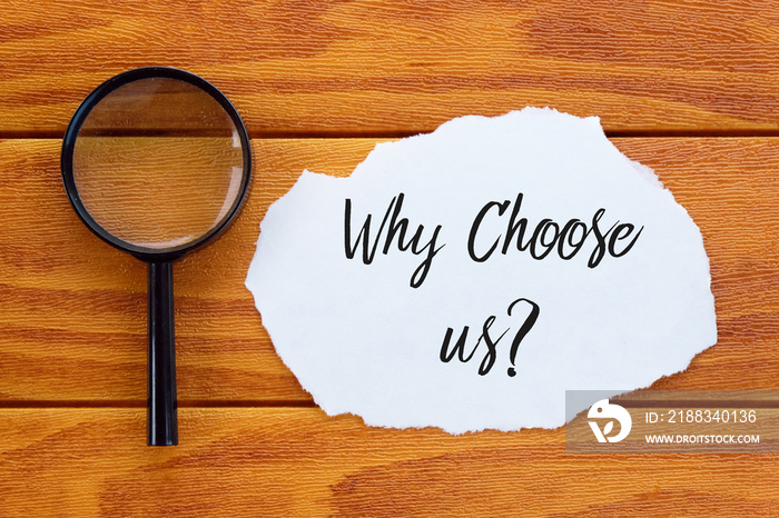 Top view of magnifying glass and piece of paper written with question Why Choose Us? on wooden backg