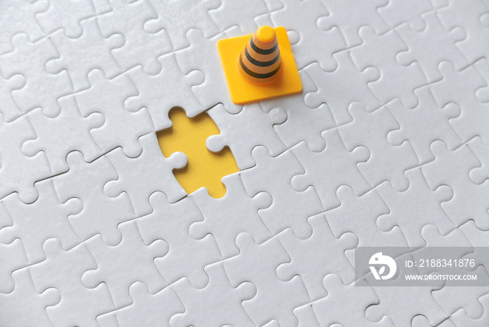 Selective focus of yellow safety cone and an empty space of white jigsaw puzzle with yellow backgrou