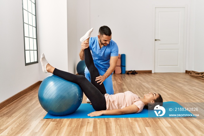 Latin man and woman wearing physiotherapist uniform having rehab session using fit ball at rehab cen