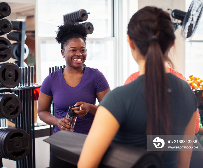 Smiling female athletes talking while standing against exercise equipment in yoga class