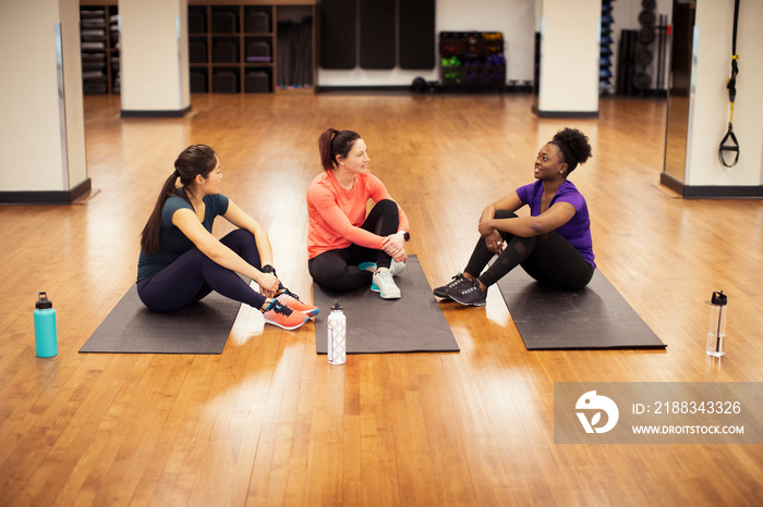 High angle view of confident female athletes talking while sitting on exercise mats in gym