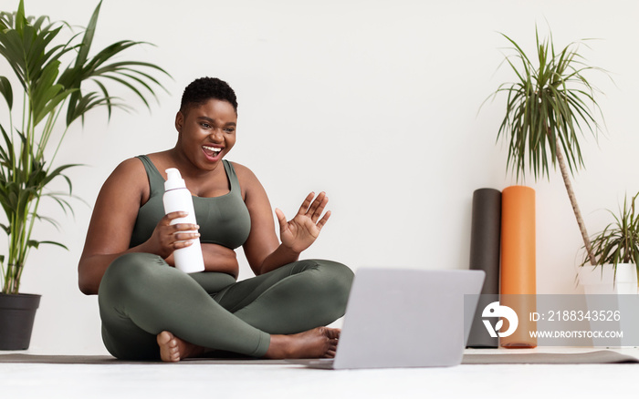 Cheerful overweight black woman having video chat with yoga coach