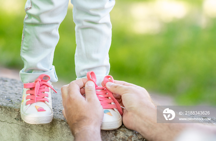 Happy family. Close up father helping her little daughter to tie shoelaces on summer day. Empty spac