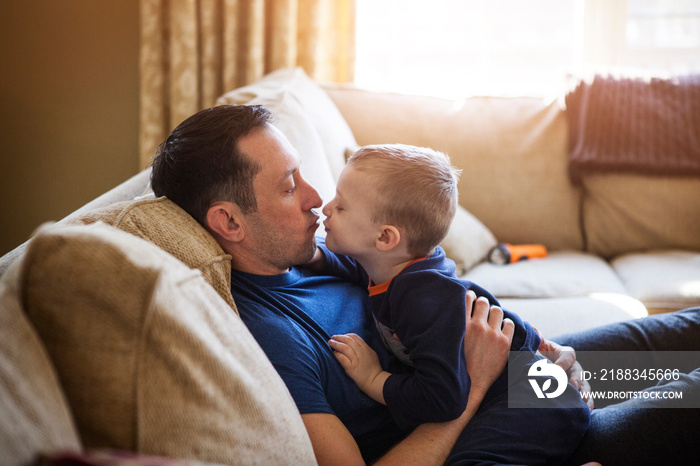 Side view of father and son kissing on sofa at home