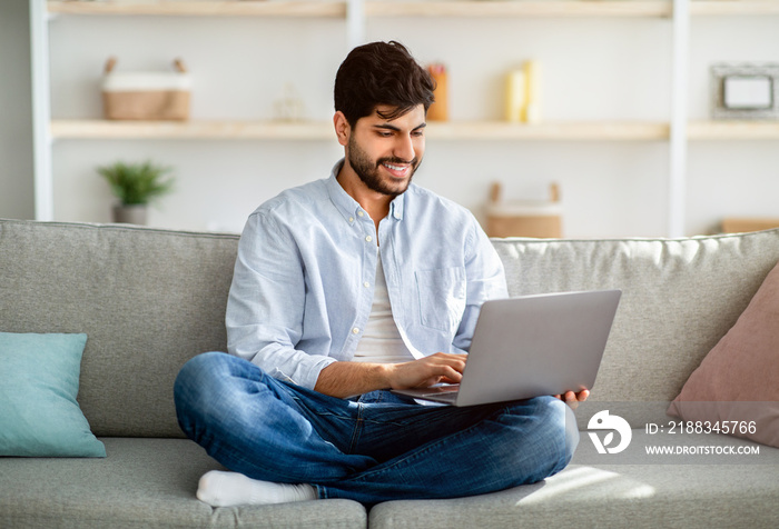 Remote work. Arab freelancer working on laptop computer at home, sitting on couch, enjoying distance