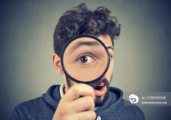 Curious amazed man looking through a magnifying glass