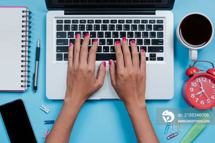 Woman hands typing on keyboard on blue desk.