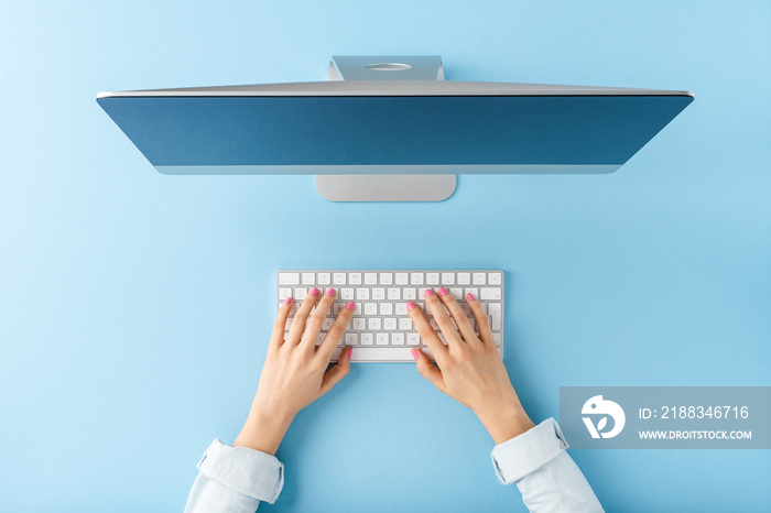 Overhead shot of woman’s hands working on computer on blue background. Office desktop. Flat lay