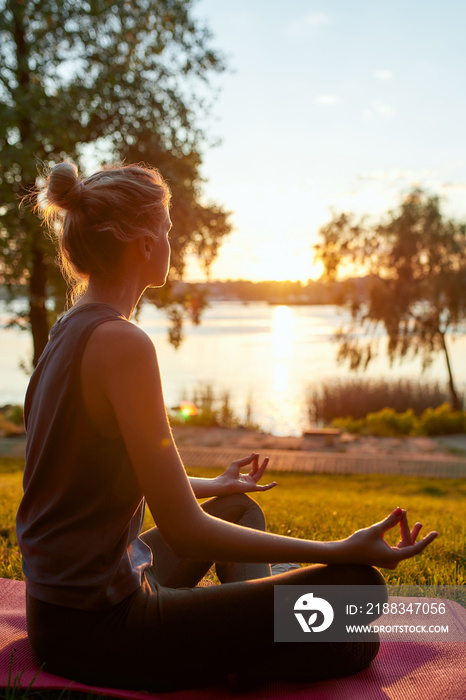 健康概念。一个女人早上在户外做瑜伽，坐在莲花姿势的垂直镜头