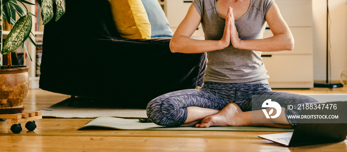 woman doing yoga workout at home watching videos online on laptop computer