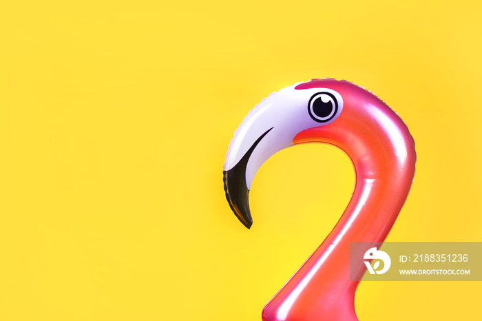 Summer fun concept with pink inflatable flamingo head on a yellow background with copy space