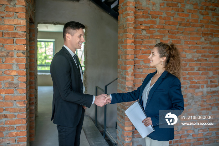 Male investor in a black suit shaking hands with the broker