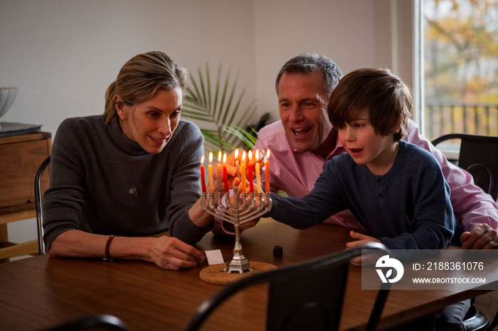Cheerful grandparents with grandson burning candles on menorah during Hanukkah festival