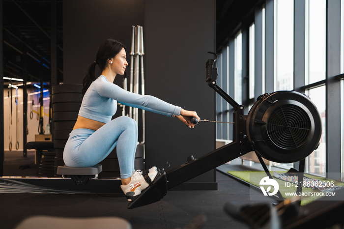 Side view of sports woman doing exercise on rowing machine