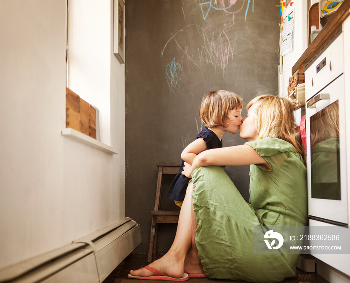 Side view of mother and daughter kissing in kitchen