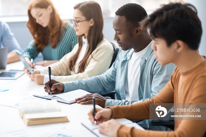 Diverse Students Sitting At Desk In Line Taking Notes