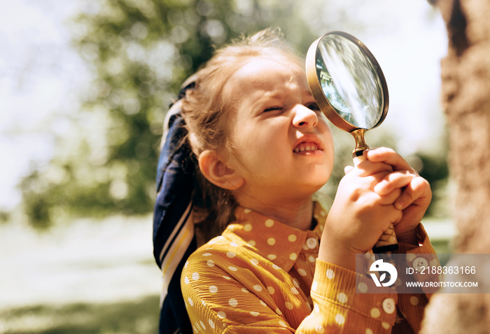 Cute little girl exploring the nature with magnifying glass outdoor. Child playing in the forest wit