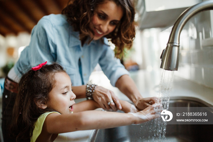 Mother with daughter washing hands in kitchen sink