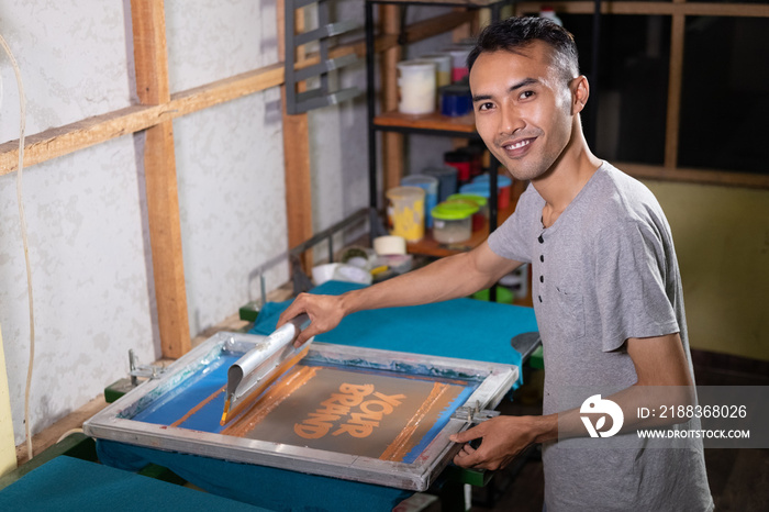 Male workers are confident in using the screen printing squeegee to print T-shirts at the workshop