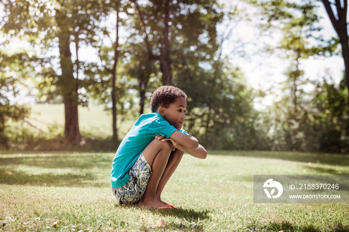 Boy (8-9) crouching in field