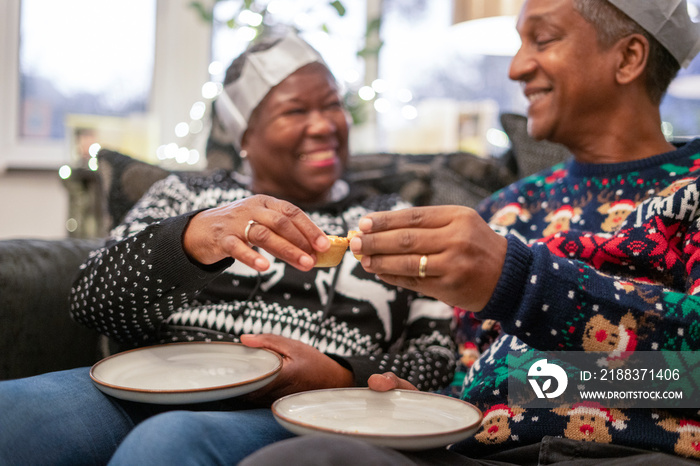 Senior couple sitting on sofa eating Christmas cookies