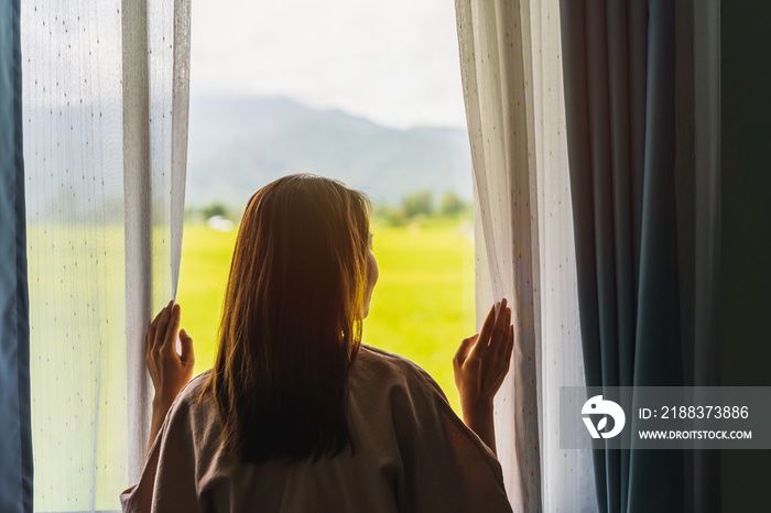 young woman opening curtains in the morning and looking through the window