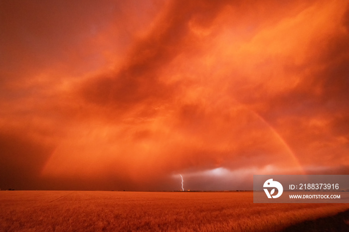 A dust storm with vivid orange sky and rainbow, and cloud-to-ground lightning strike.