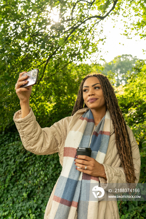 Smiling woman in coat taking�selfie�in park in autumn