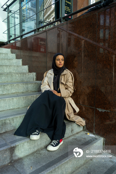 Young woman wearing�hijab sitting outside office building