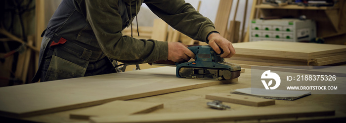 Close up. Carpenter at workshop polishes wooden board with a electric orbital sander. Woodwork and f