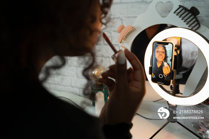 Teenage girl applying lip gloss while filming makeup video at home