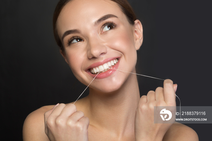 Portrait of excited cute girl is standing and using dental floss for cleaning teeth. She is looking 