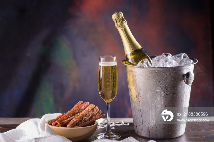 Champagne bottle in bucket with ice and glasses of champagne on dark background