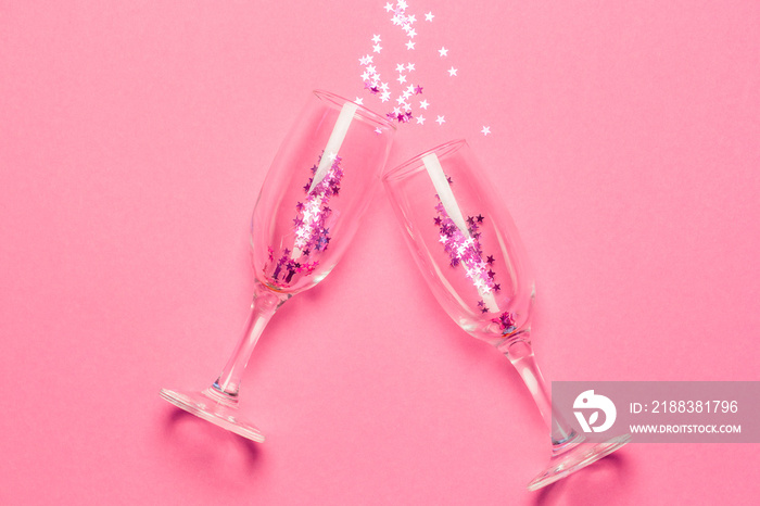 两个香槟酒杯，粉红色背景上点缀着粉红色星星形状的五彩纸屑。俯视图。淡水河谷