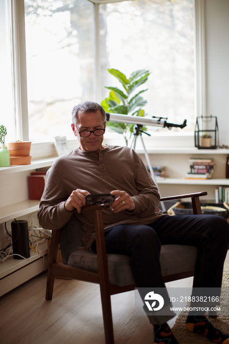 Mature man using mobile phone while sitting on chair at home