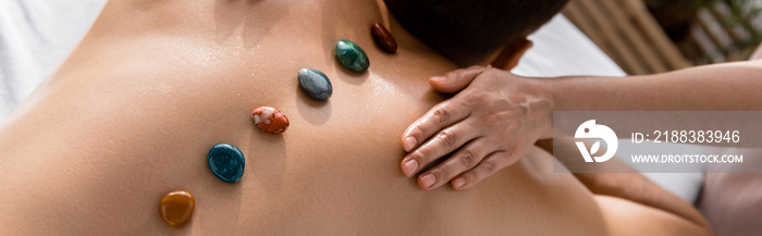 panoramic shot of masseur and shirtless man with stones on back