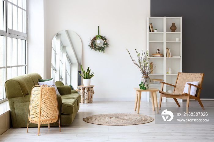 Stylish interior of living room with sofa, armchair and Easter wreath on light wall