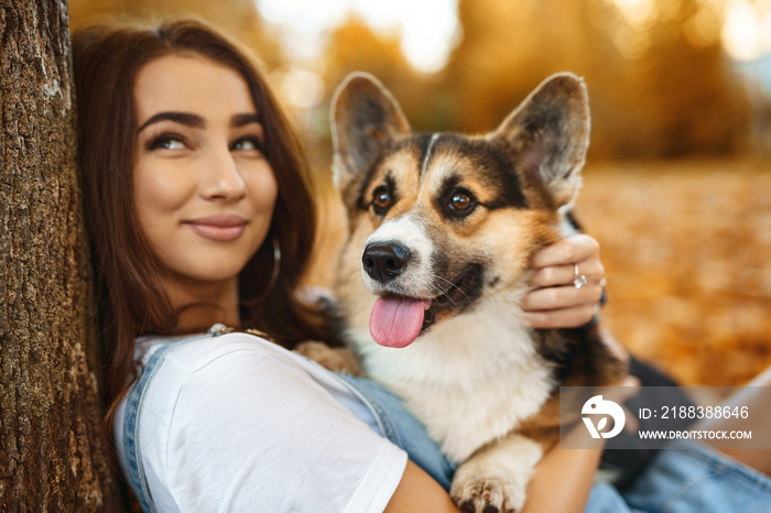 微笑快乐的女人和威尔士柯基彭布罗克犬在户外公园里。年轻的女主人hu