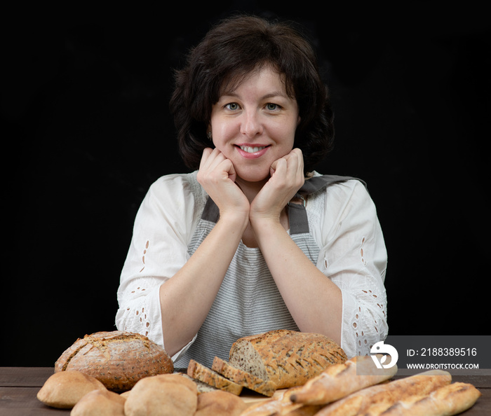 Portrait of female baker with different breads. Isolated on dark background