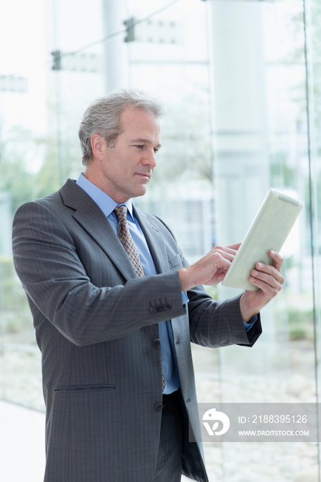 Mature corporate businessman using digital tablet at office window